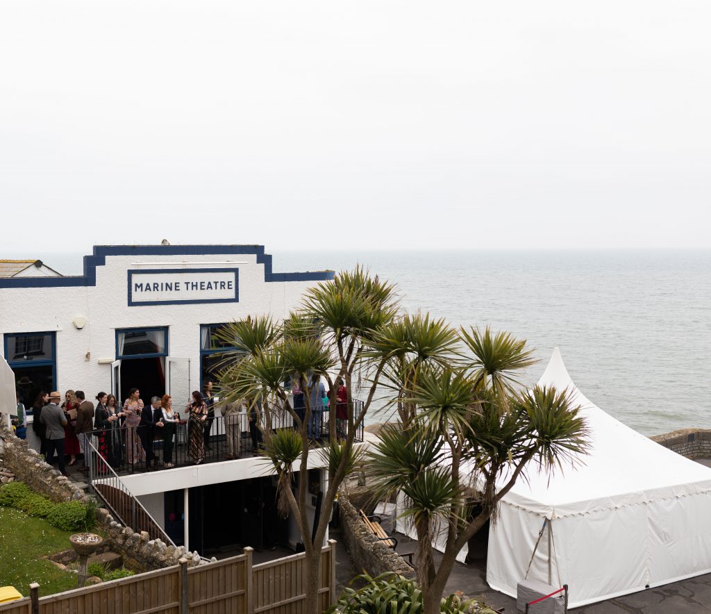 Marine Theatre (Dorset) wedding guests stood on the large balcony chatting and looking at the sea.