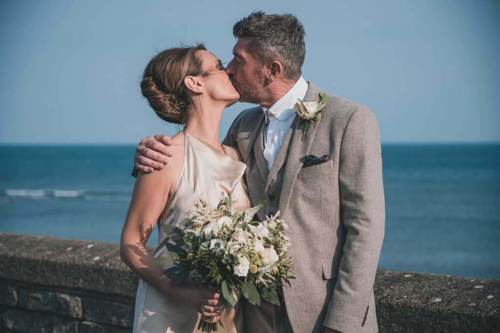 Wedding couple kissing in front of the sea at the Marine Theatre, Lyme Regis, Dorset.