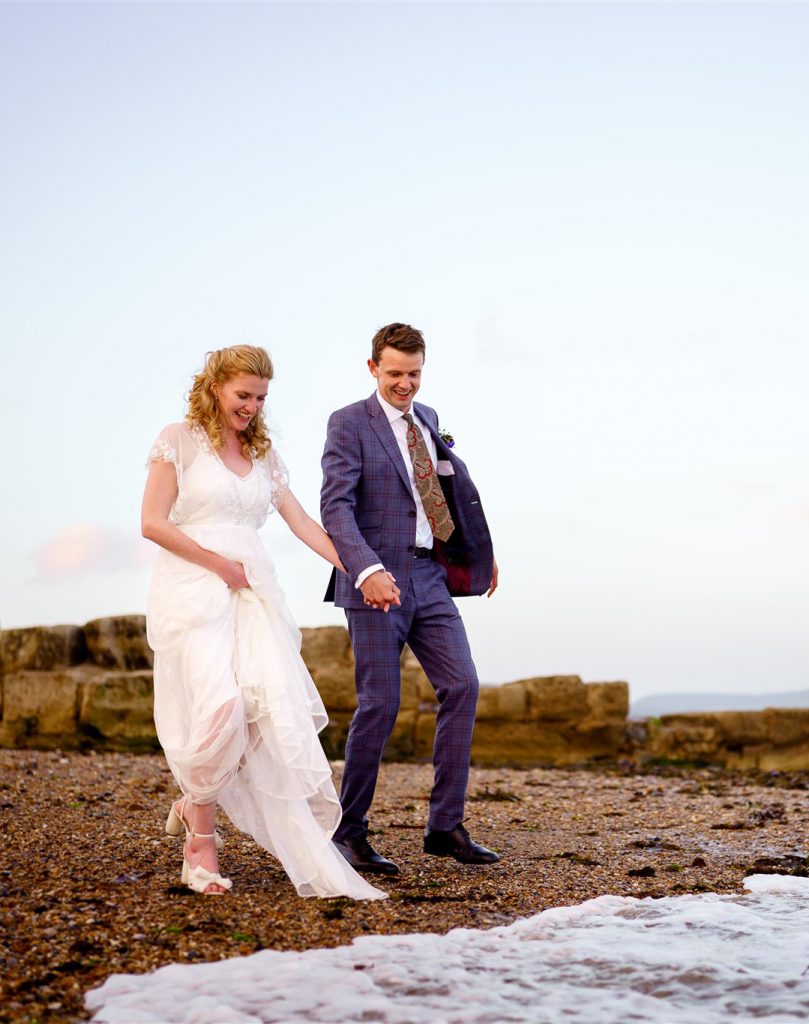 Wedding couple running into the waves on Lyme Regis beach, Dorset.