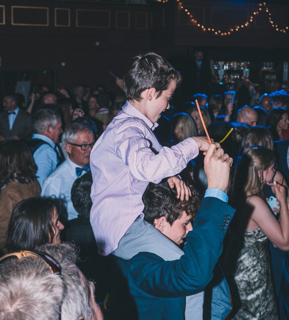 Young boy on mans shoulders holding a glow stick at a wedding reception in the Marine Theatre (South West of England).